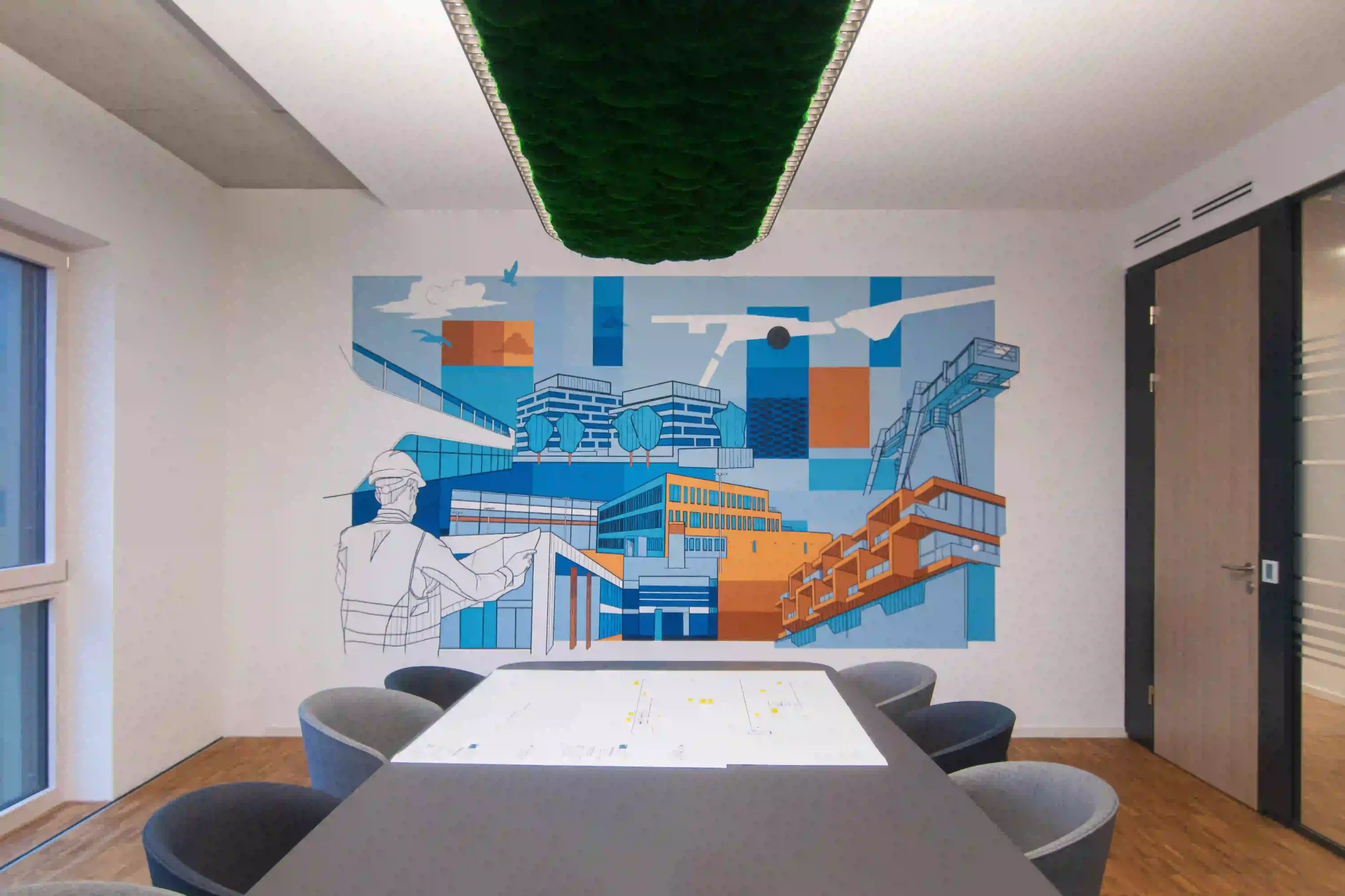 Architektonisches Wandbild in einem Besprechungsraum mit stilisierten Gebäuden, einem Bauarbeiter und industriellen Elementen in Blau- und Orangetönen.